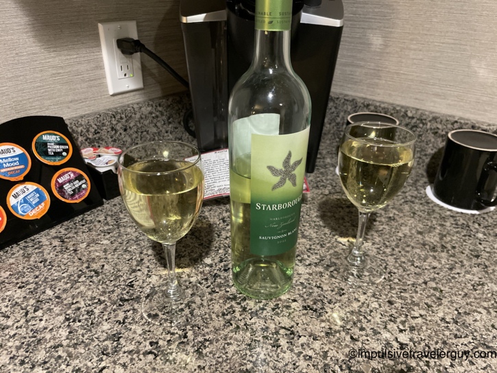 Bottle of Starborough Marlborough New Zealand Sauvignon Blanc on a granite counter with two filled wine glasses, beside a Keurig machine and Maud's coffee pods