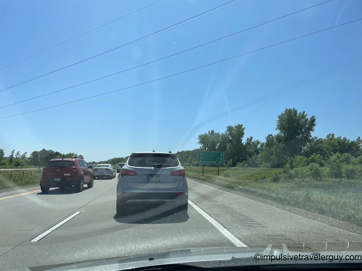 Highway traffic from behind wheel following silver SUV closely with red vehicle in passing lane, green roadside vegetation visible