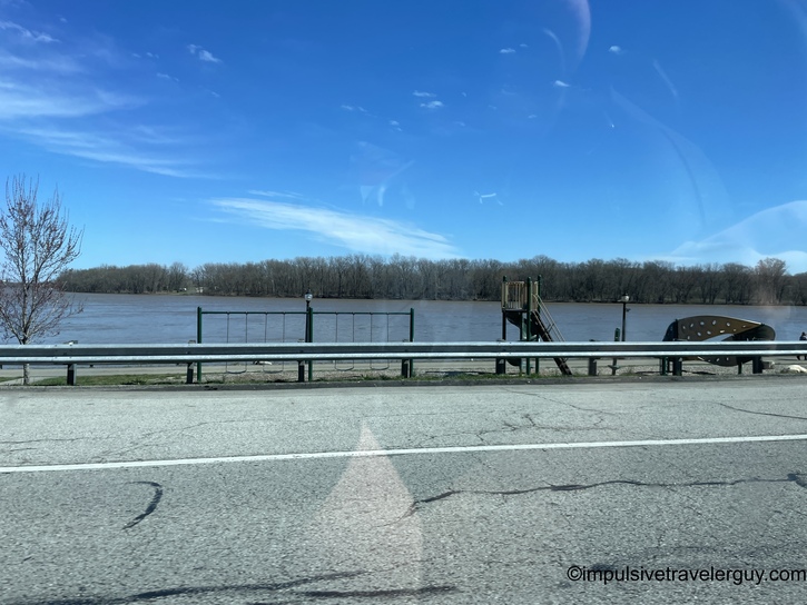 River view with boat launch facility, wooden dock structure, and guardrail along shoreline under blue sky