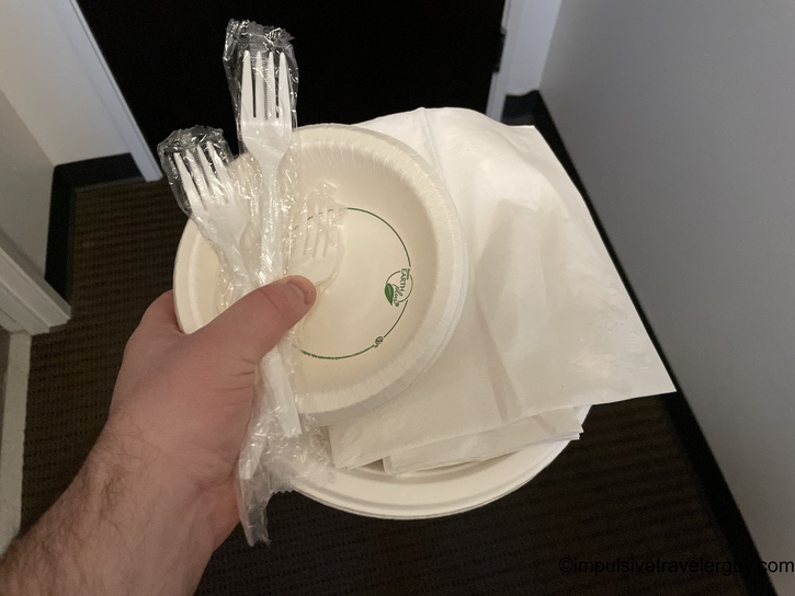 Hand holding compostable plate and wrapped plastic utensils with green certification logo visible