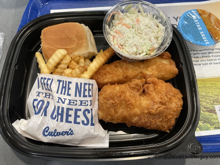 Culver's restaurant meal tray containing fried fish, french fries, coleslaw, a bun, and tartar sauce on a black plastic tray with branded napkin