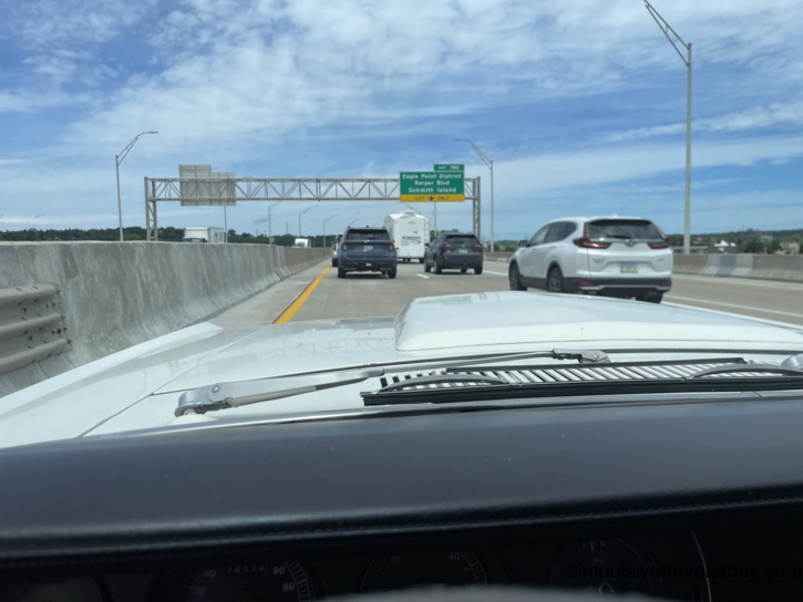 Heading back east across the Dubuque bridge in the Cougar, merging with highway traffic past the Exit 190 sign for Eagle Point District, Kerper Blvd, and Schmitt Island, concrete jersey barriers lining the left lane.
