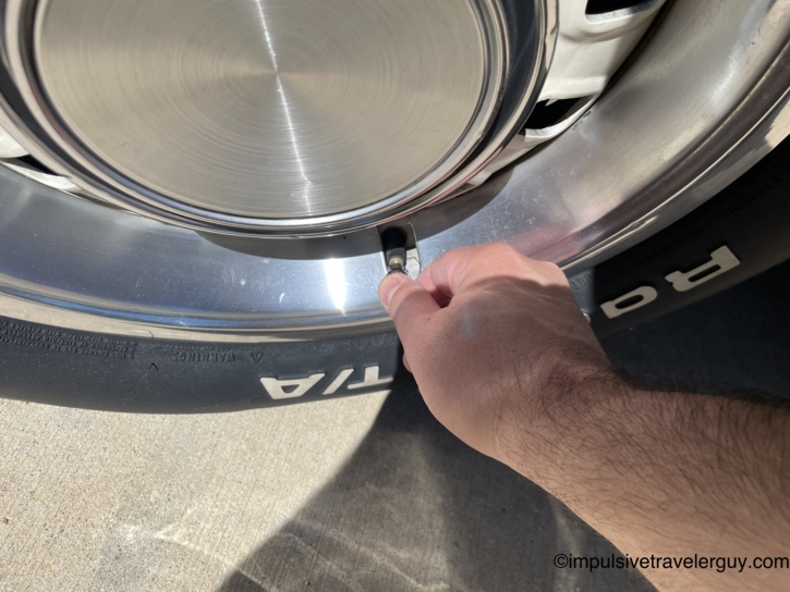 A hand checking tire pressure on the Cougar's BFGoodrich Radial T/A tire, reaching for the valve stem past the polished aluminum center cap and chrome wheel.