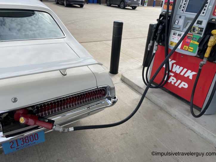 The Cougar's rear at a second Kwik Trip stop, fuel nozzle in the filler, Wisconsin collector plate 213800 visible below the chrome-louvered tail panel.