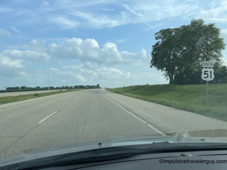 Driving south on US Highway 51 through flat open farmland under partly cloudy summer skies.