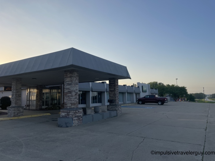 Budget motel exterior with stone-pillared porte-cochere entrance and a lone pickup truck at dusk.