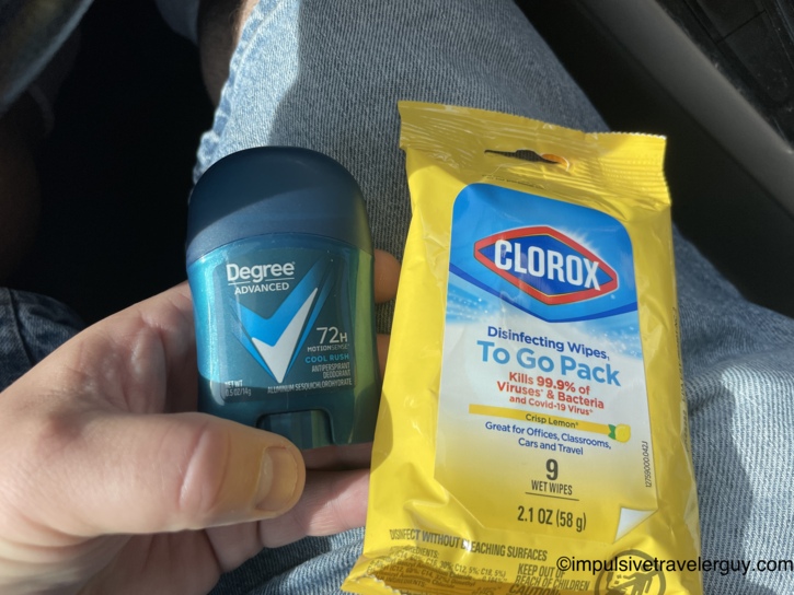 Hand holding a travel-size Degree Advanced Cool Rush deodorant next to a Clorox Disinfecting Wipes To Go Pack on a denim-covered lap in the car.