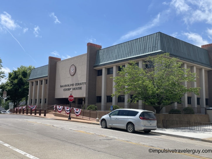 Randolph County Court House, a modern brutalist-style concrete and brick building with a green metal roof, patriotic bunting along the railing, and county seal on the facade.