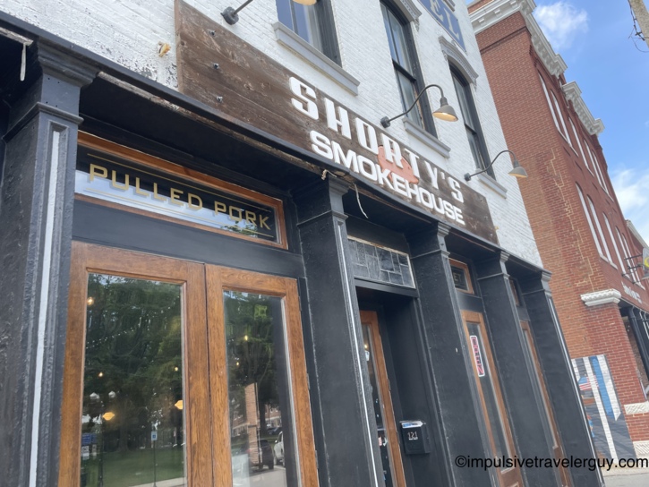 Shorty's Smokehouse storefront with black-painted facade, gold Pulled Pork lettering in the window, rustic wood signage, and gooseneck light fixtures on a historic downtown block.