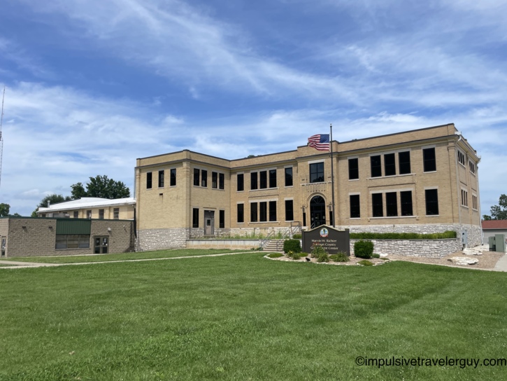 Marvin W. Richter Calhoun County Government Center, a two-story yellow brick building with arched entrance, stone foundation, American flag, and manicured lawn.