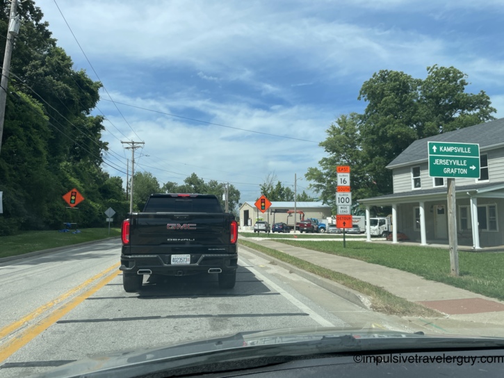 Stopped behind a black GMC Sierra Denali at an intersection in a small Illinois town with signs for Kampsville, Jerseyville, Grafton, Illinois Route 16 East, and Illinois Route 100 South with detour warnings.