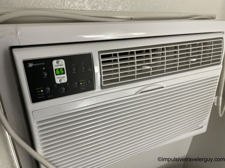 Close-up of the same Seasons wall AC unit powered on and set to 65 degrees in Cool mode with the green LED display lit.