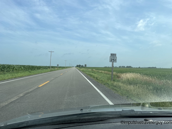Driving north on Illinois Route 251 through flat cornfield country with power lines and overcast sky.