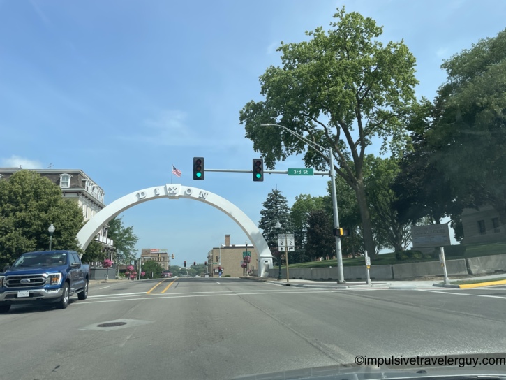 Downtown Dixon, Illinois with the iconic white memorial arch spanning the main street, traffic lights at 3rd Street, and historic buildings on both sides.