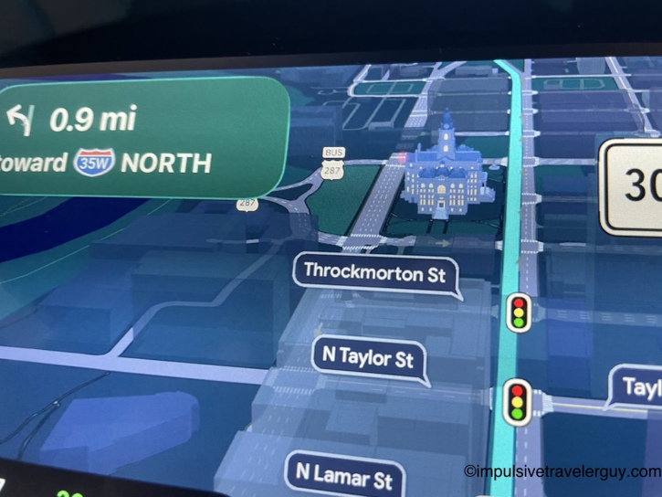 Car dashboard Google Maps screen displaying a 3D model of the historic Fort Worth courthouse while navigating downtown.