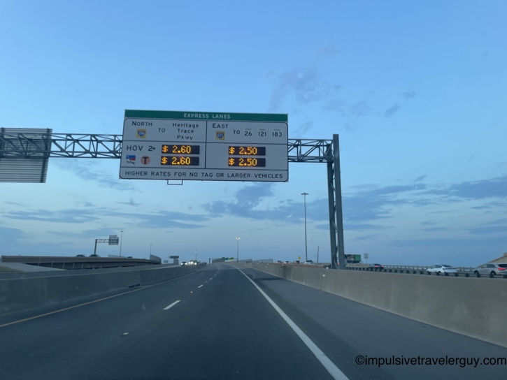 Driving on an open highway at dusk, approaching an overhead electronic sign for Express toll lanes.