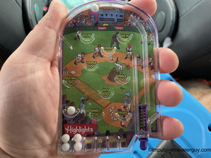 A hand holding a kid's meal prize from Braum's, a small handheld pinball game with a baseball theme.
