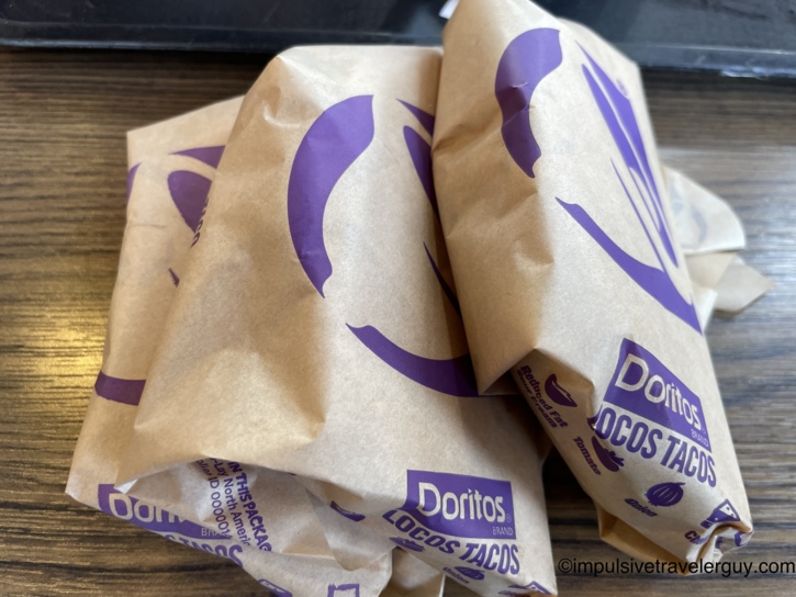 Three Taco Bell Doritos Locos Tacos wrapped in branded paper packaging sitting on a table.