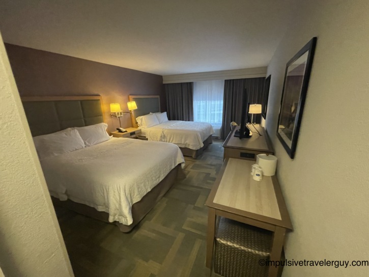 Interior of a Hampton Inn hotel room featuring two beds packed tightly together in a smaller space.