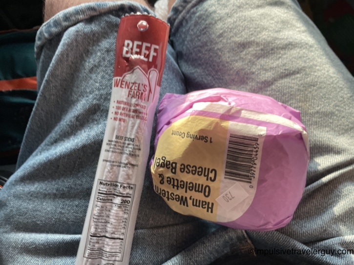 A Wenzel's Farm beef stick and a foil-wrapped breakfast sandwich resting on a lap inside the vehicle.
