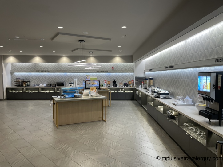 A large, well-stocked hotel breakfast area featuring a long serving counter with food warmers, a central island, and a juice machine.
