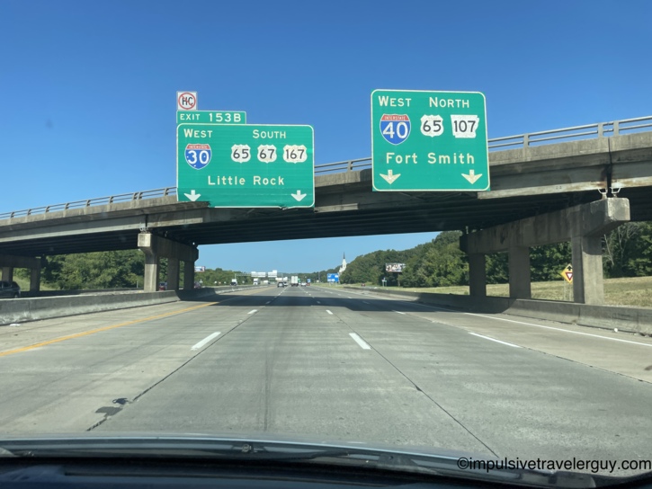 View from a car approaching a highway overpass with green signs directing traffic to Interstate 30 West towards Little Rock and Interstate 40 West towards Fort Smith.