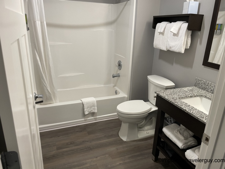 A hotel bathroom containing a white bathtub and shower combo, a toilet, and a dark wood vanity.