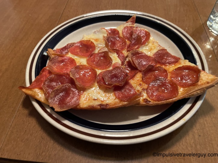 A large slice of pepperoni pizza resting on a plate on a wooden table during supper at the grandparents' house.