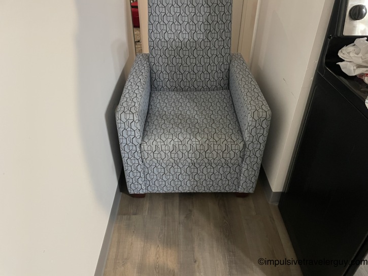 A patterned armchair wedged into a narrow space next to a kitchen appliance to act as a makeshift barricade for the play area.