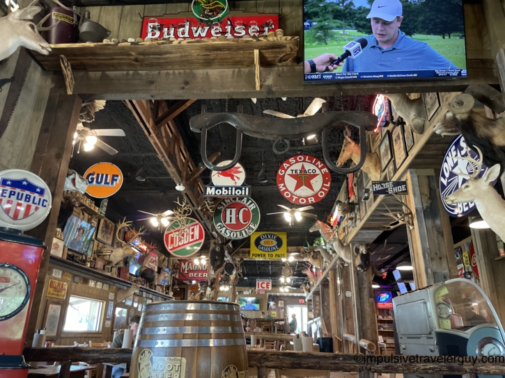 Interior of the Chicken Oil Co. restaurant densely decorated with vintage oil and gas signs, taxidermy mounts, and a large wooden barrel.