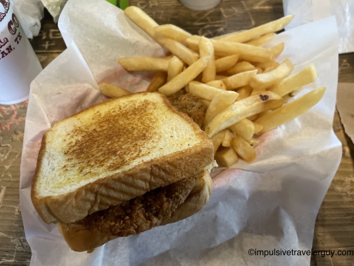 A chicken fried steak sandwich served on toasted bread alongside thick-cut french fries resting on paper wrapping.
