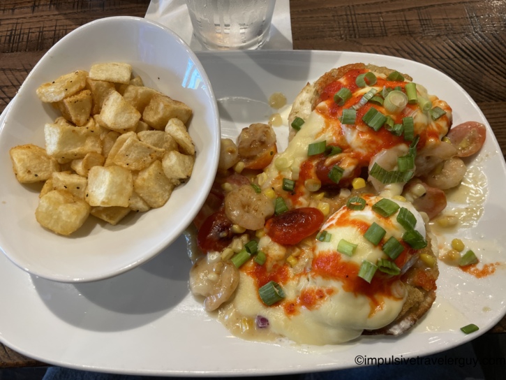 A plate holding a shrimp eggs benedict breakfast dish served alongside a bowl of diced breakfast potatoes from Another Broken Egg.