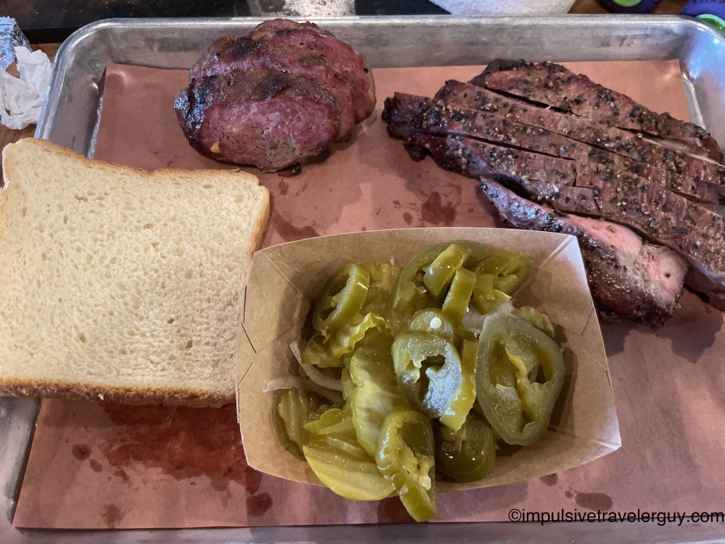 A metal tray lined with butcher paper holding a Southside Market barbecue meal including smoked steak, a Sausage Slammer, white bread, and pickled jalapeños.