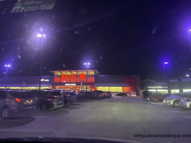 Nighttime view looking across a busy parking lot at a brightly lit H-E-B grocery store.