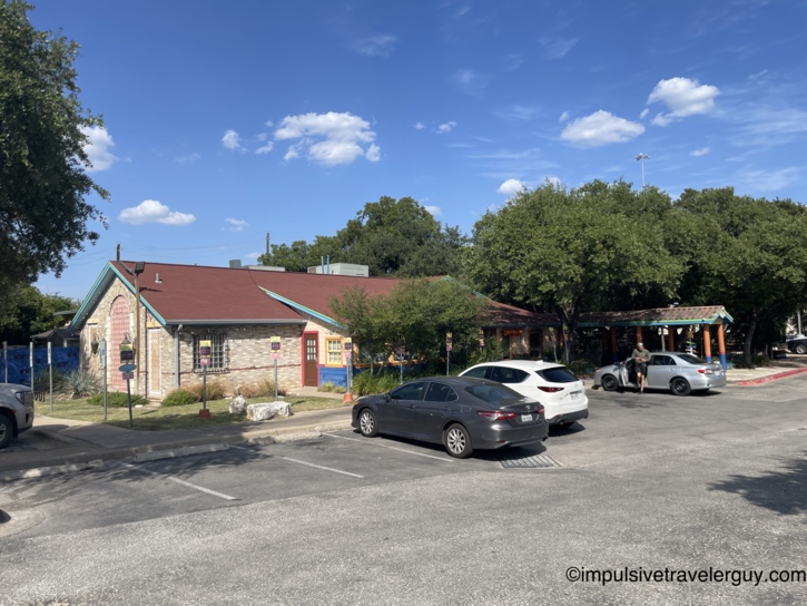 Exterior view of a Chuy's restaurant building with a red shingle roof and colorful painted trim on a sunny day.