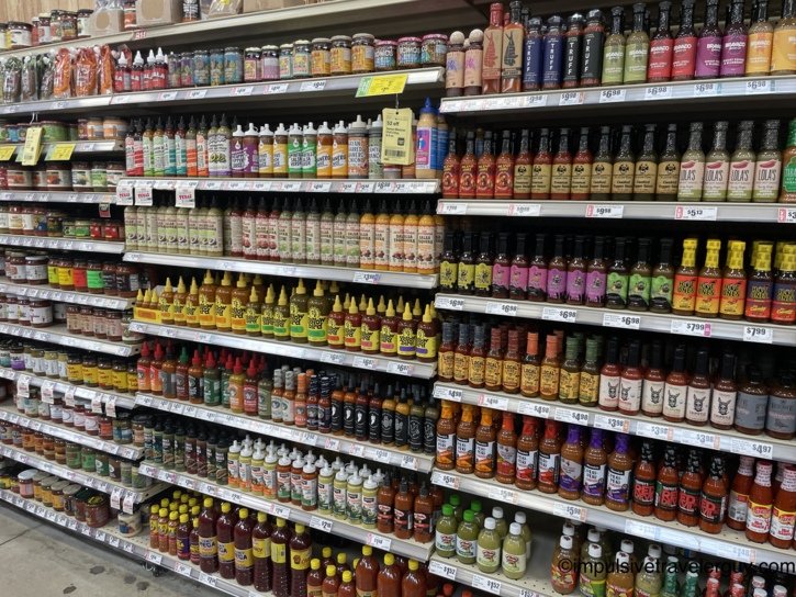 Long grocery store shelves at H-E-B densely packed with a massive variety of bottled hot sauces.