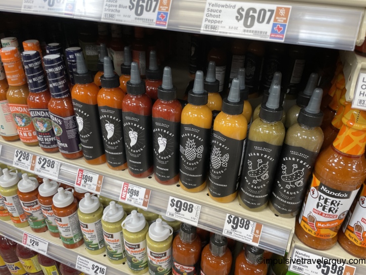 Close-up of an H-E-B shelf stocked with a row of black-labeled Heartbeat Hot Sauce bottles.