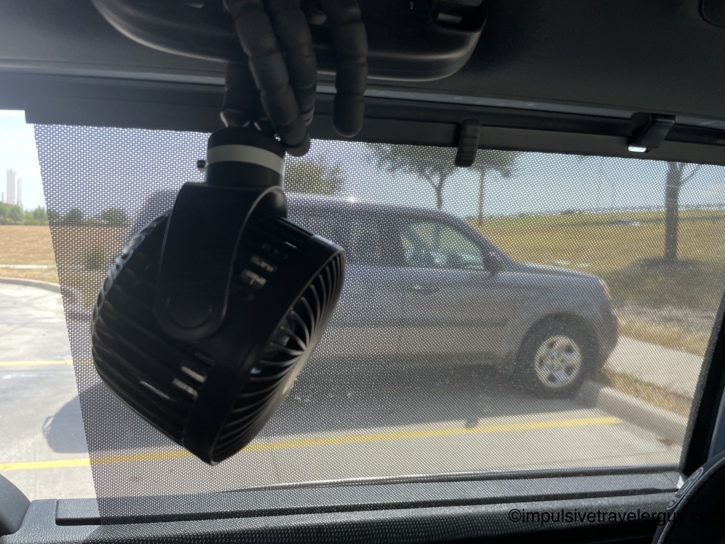 Interior of the van showing a small black battery-powered fan mounted above a sun-shaded side window.