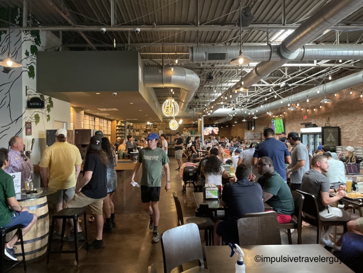 Wide view of the bustling interior at Maple Branch Craft Brewery filled with patrons sitting at tables and standing near the bar.
