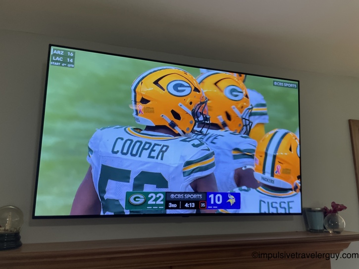 A flat-screen television mounted above a wooden mantel, broadcasting a Green Bay Packers football game.